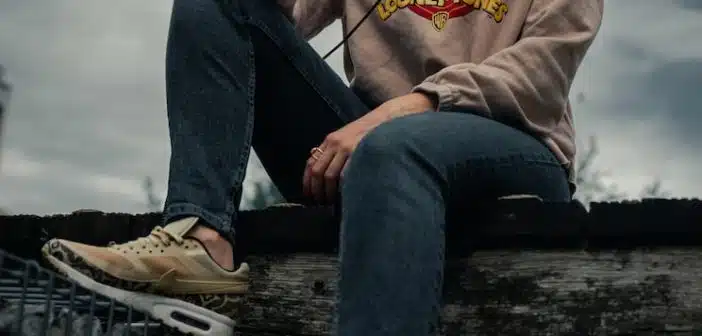 woman in gray hoodie and blue denim jeans sitting on wooden bench